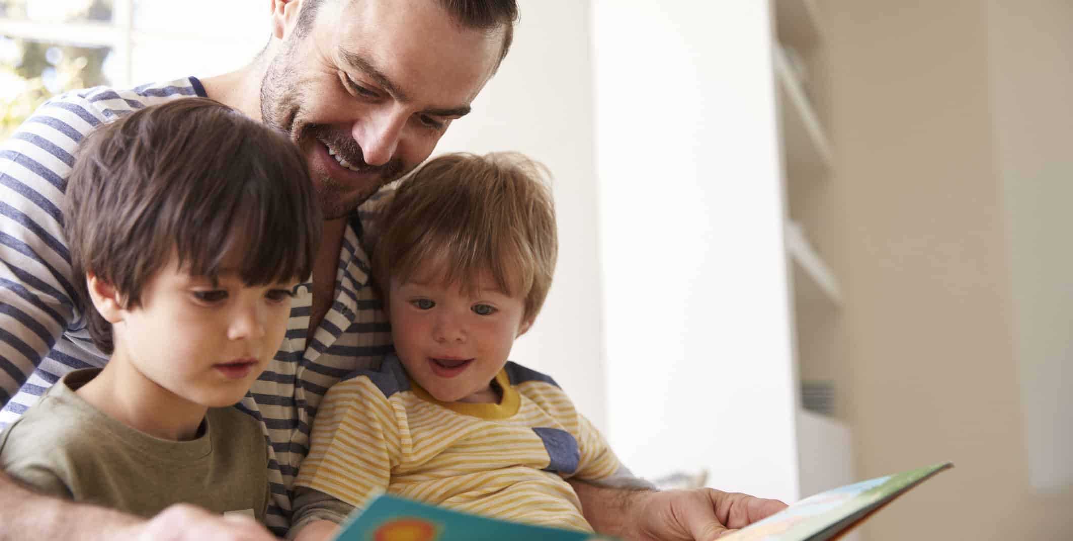 Close Up Of Father And Sons Reading Story At Home Together