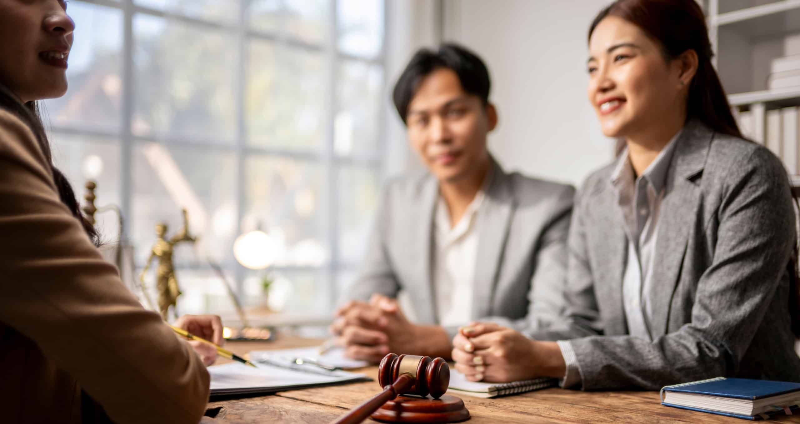 A woman and a man are sitting at a table with a judge. The woman is smiling and the man is looking at her